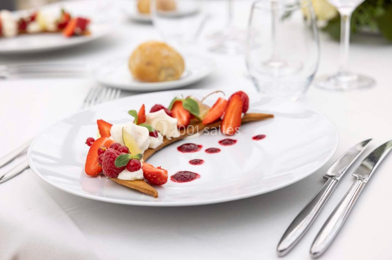 Assiette de dessert avec fruits rouges, crème et biscuits, présentée sur une table dressée avec couverts et verre.