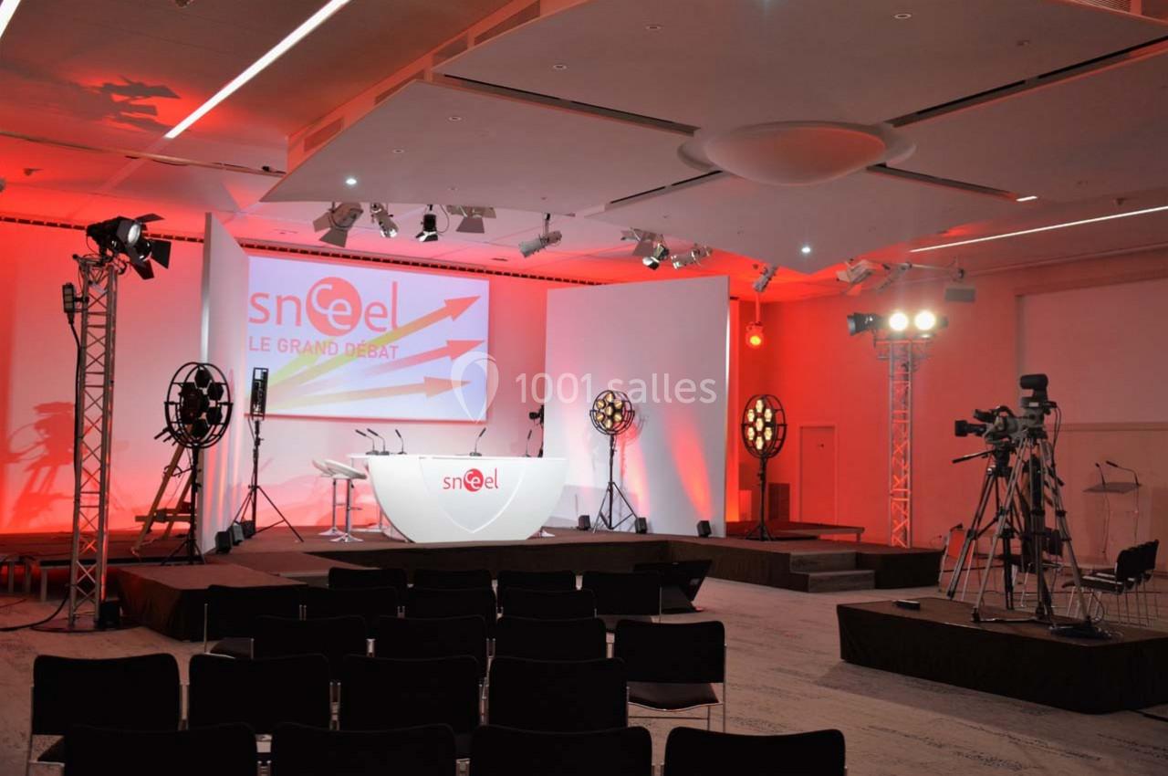 Salle de conférence équipée de projecteurs, caméras et écran de projection avec un pupitre sur scène.