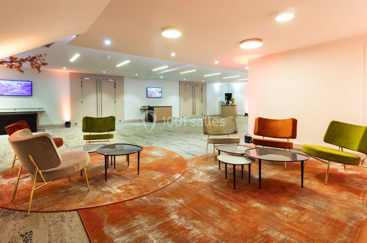 Espace lounge avec fauteuils colorés, tables basses et éclairage moderne dans un intérieur lumineux.