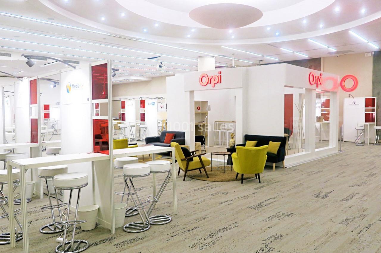 Espace intérieur lumineux avec mobilier moderne, comprenant des tables hautes, des chaises et des fauteuils colorés.