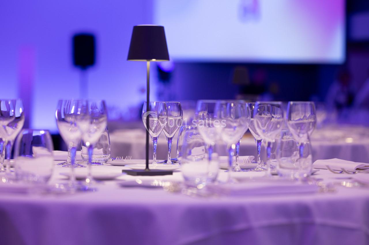 Tables élégamment dressées avec des verres en cristal et des lampes d'appoint dans une ambiance lumineuse tamisée.