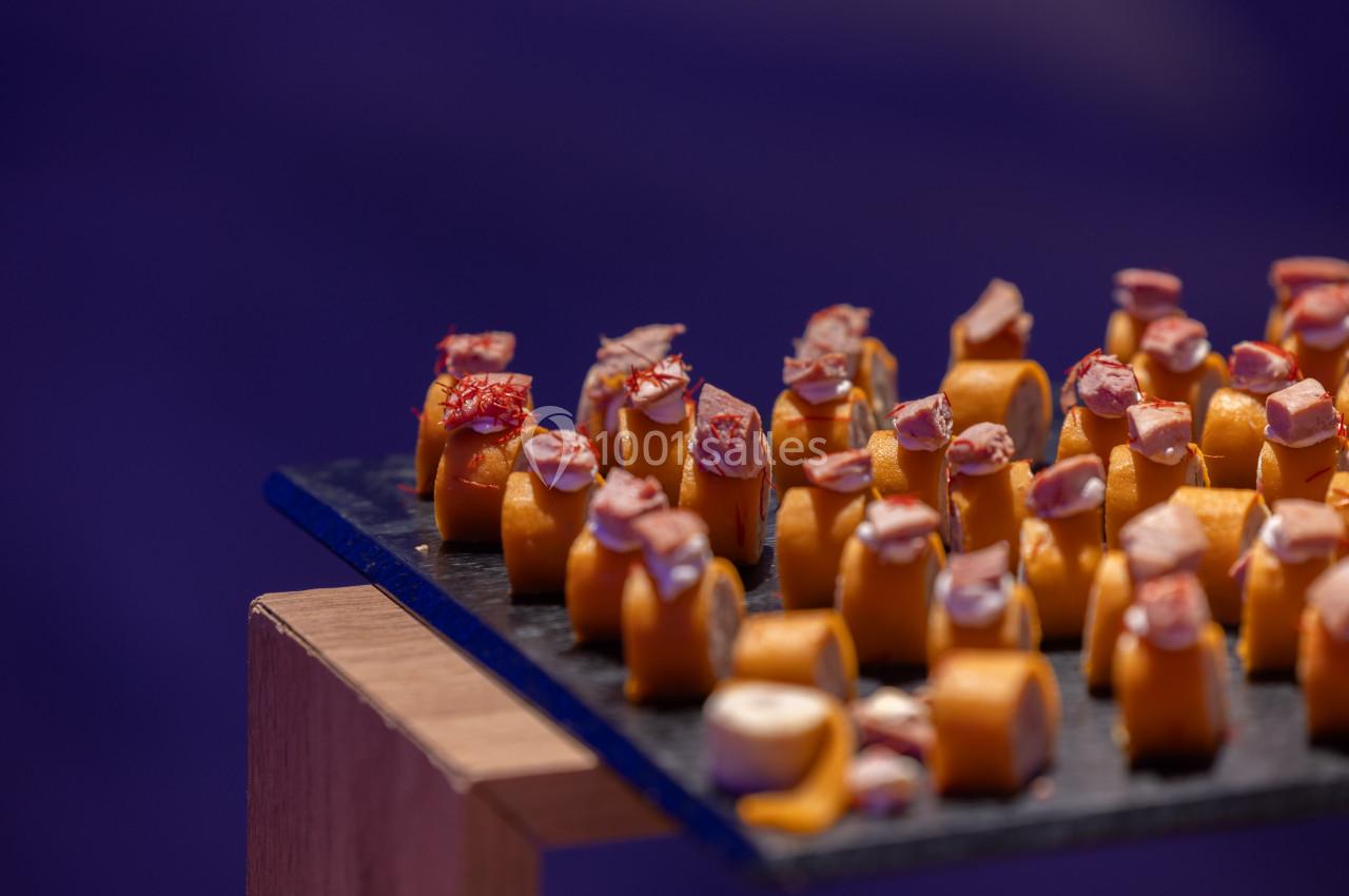 Assortiment de bouchées apéritives disposées sur une ardoise noire, avec un fond violet flou.