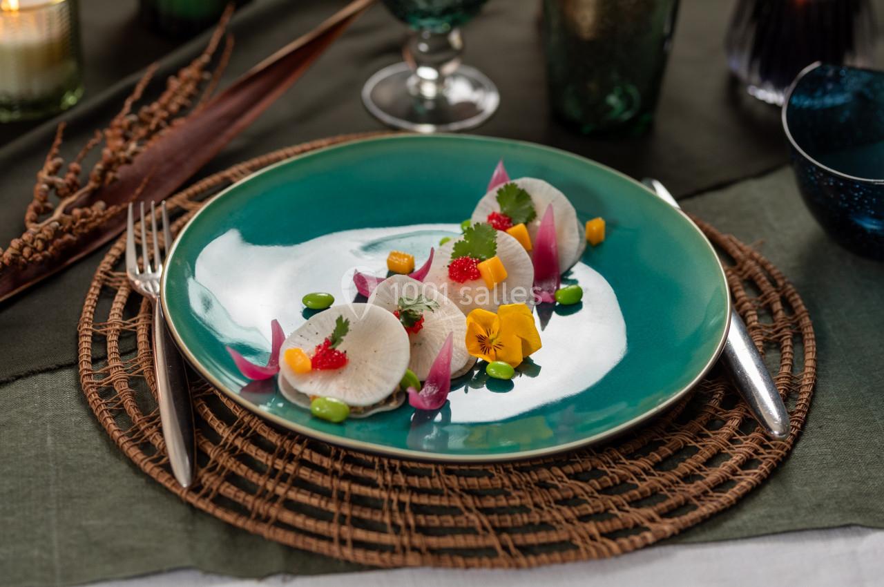 Assiette gastronomique avec radis finement tranchés, fleurs comestibles et garnitures colorées sur une table élégante.