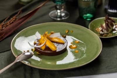 Dessert au chocolat garni de mangue, copeaux de noix de coco et pistaches, présenté sur une assiette verte.