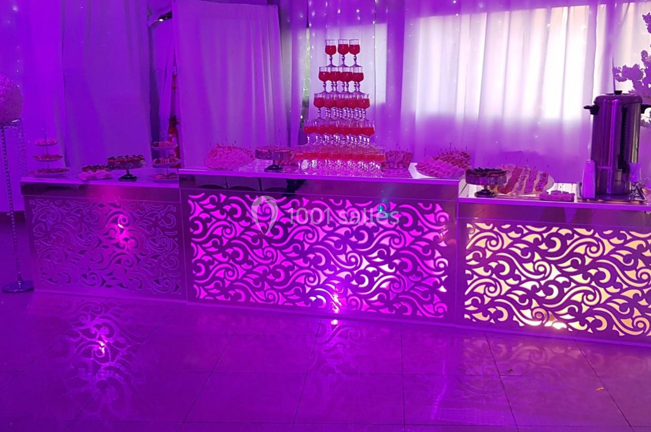 Buffet décoratif éclairé en violet avec des motifs ajourés, comprenant desserts et fontaine à boissons.