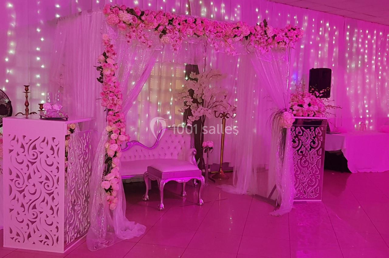 Décor de mariage avec arche fleurie, rideaux lumineux, canapé blanc et mobilier orné dans une ambiance rose.