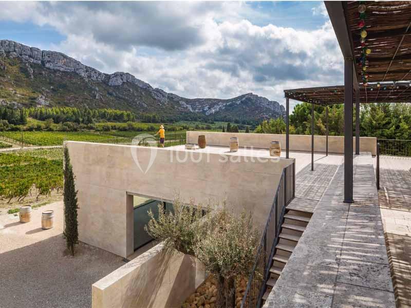 Terrasse moderne surplombant un paysage de vignobles, montagnes et ciel partiellement nuageux en arrière-plan.