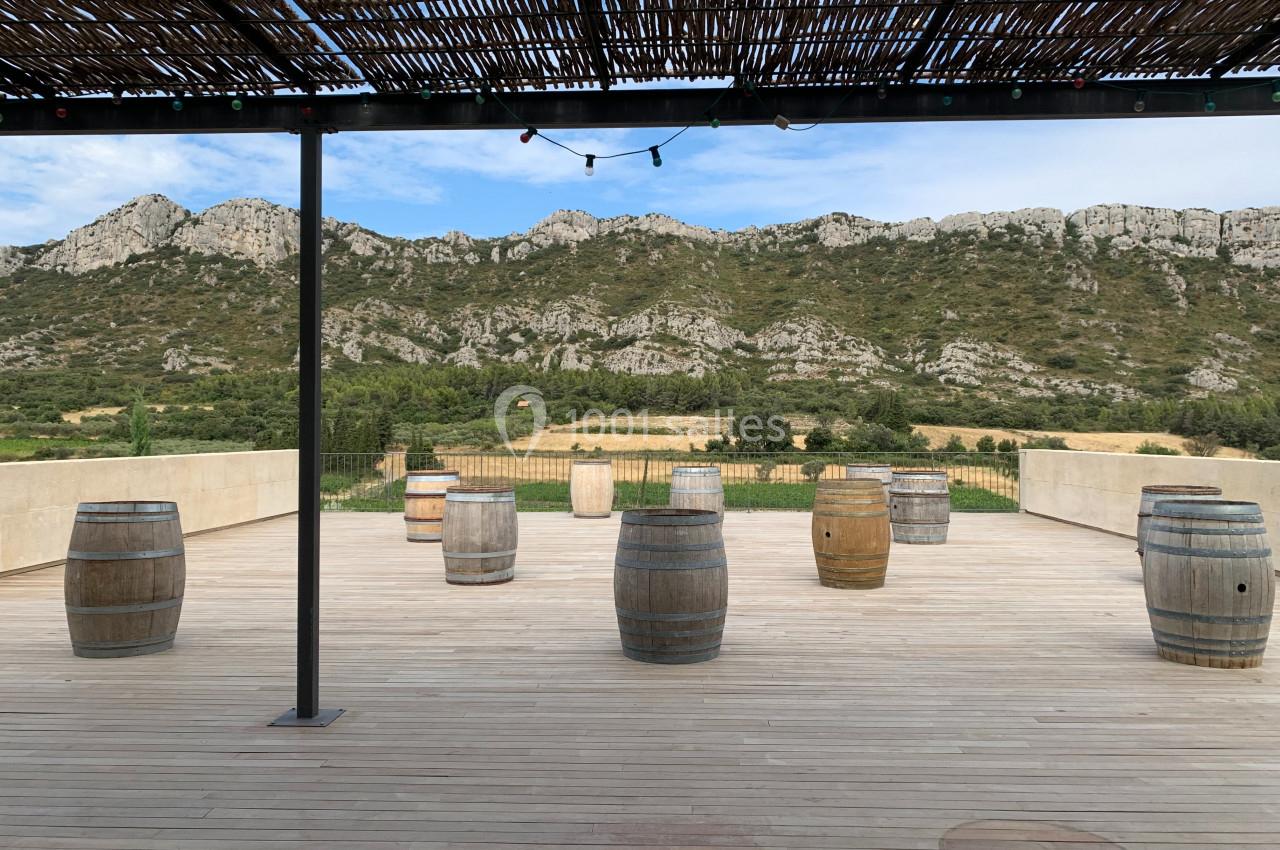 Terrasse en bois avec des tonneaux dispersés, vue sur des collines rocheuses et ciel partiellement nuageux.