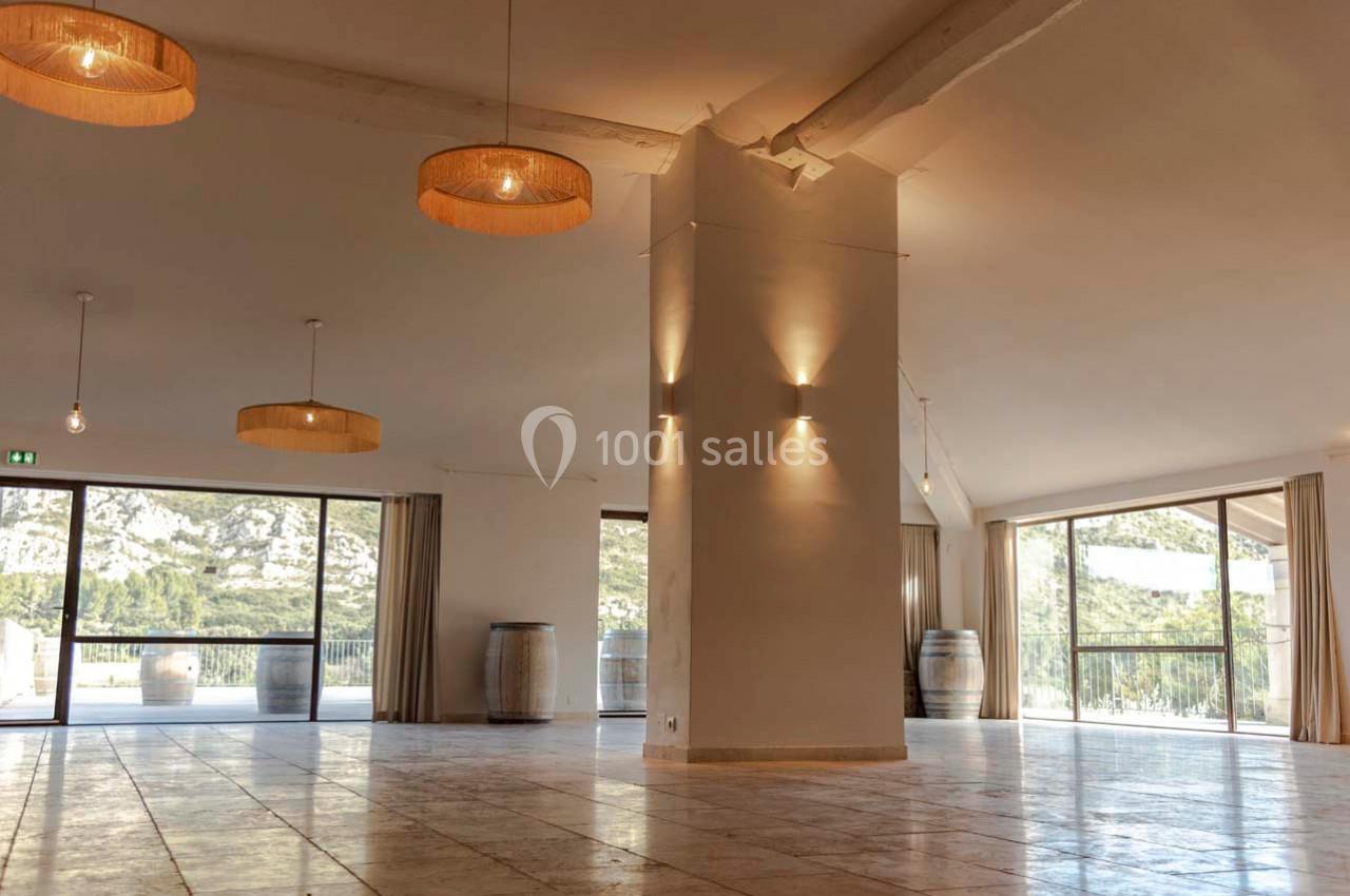 Salle lumineuse avec de grandes baies vitrées, murs clairs, poutres apparentes et suspensions en osier.