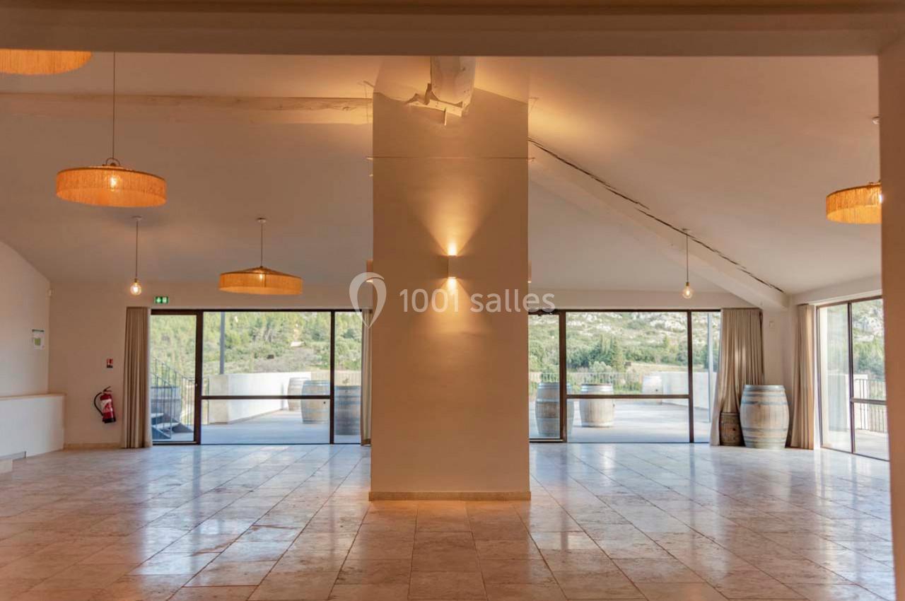 Salle lumineuse avec un sol en carrelage clair, des suspensions en osier et de grandes baies vitrées donnant sur l'extérieur.