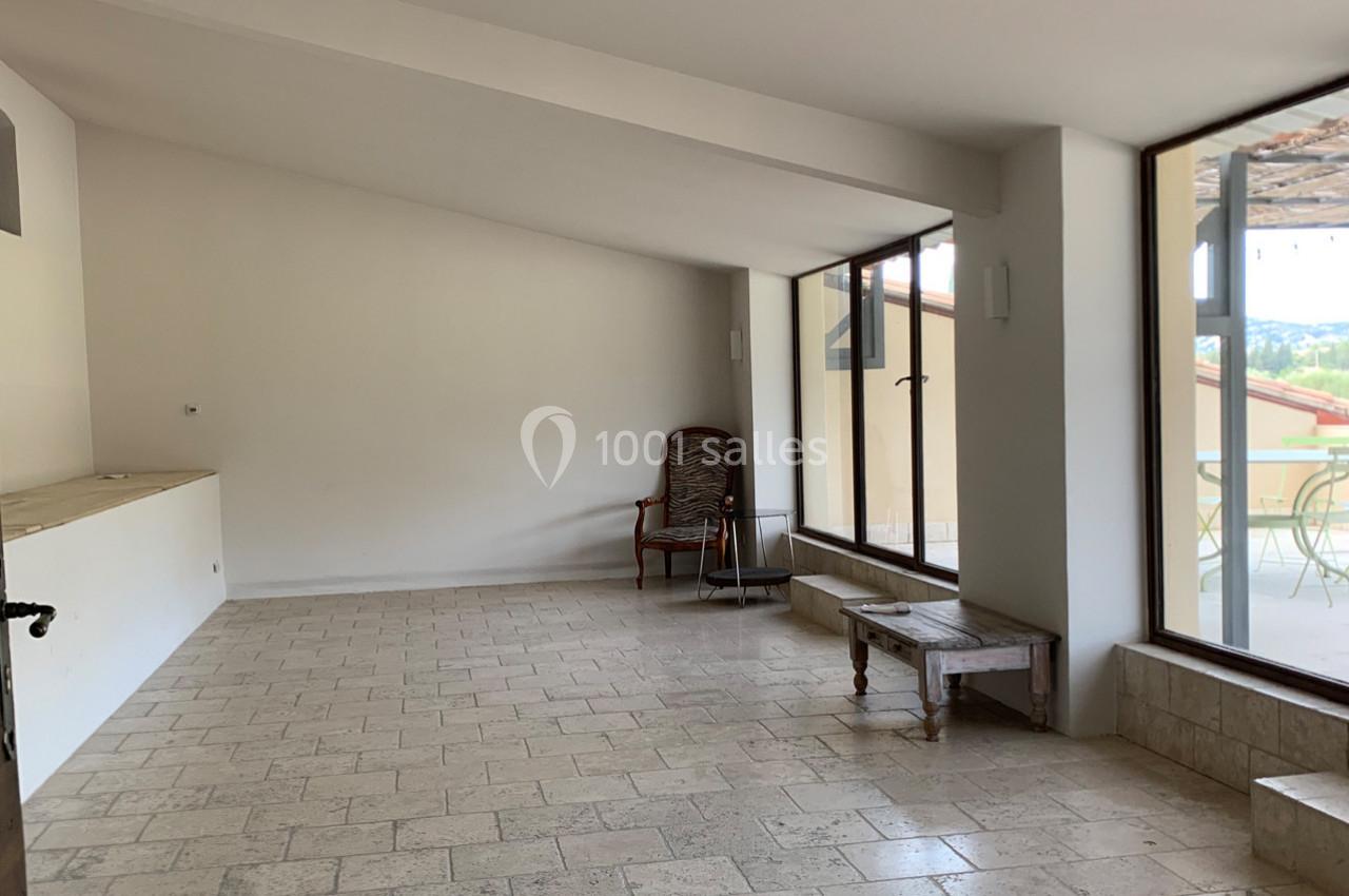 Salle lumineuse avec carrelage clair, murs blancs, chaise en osier, table basse en bois et grandes baies vitrées donnant sur…