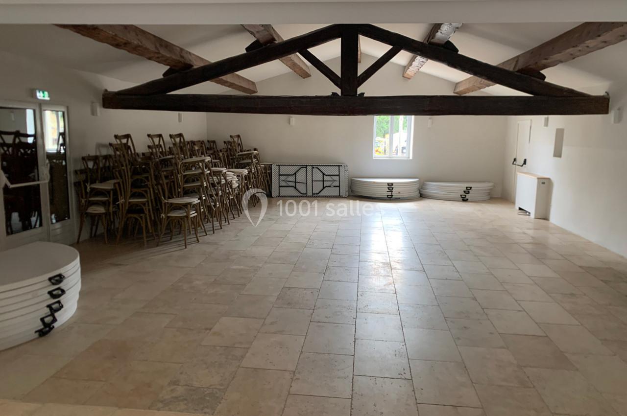 Salle vide avec sol en carrelage, poutres apparentes, tables et chaises empilées contre les murs.