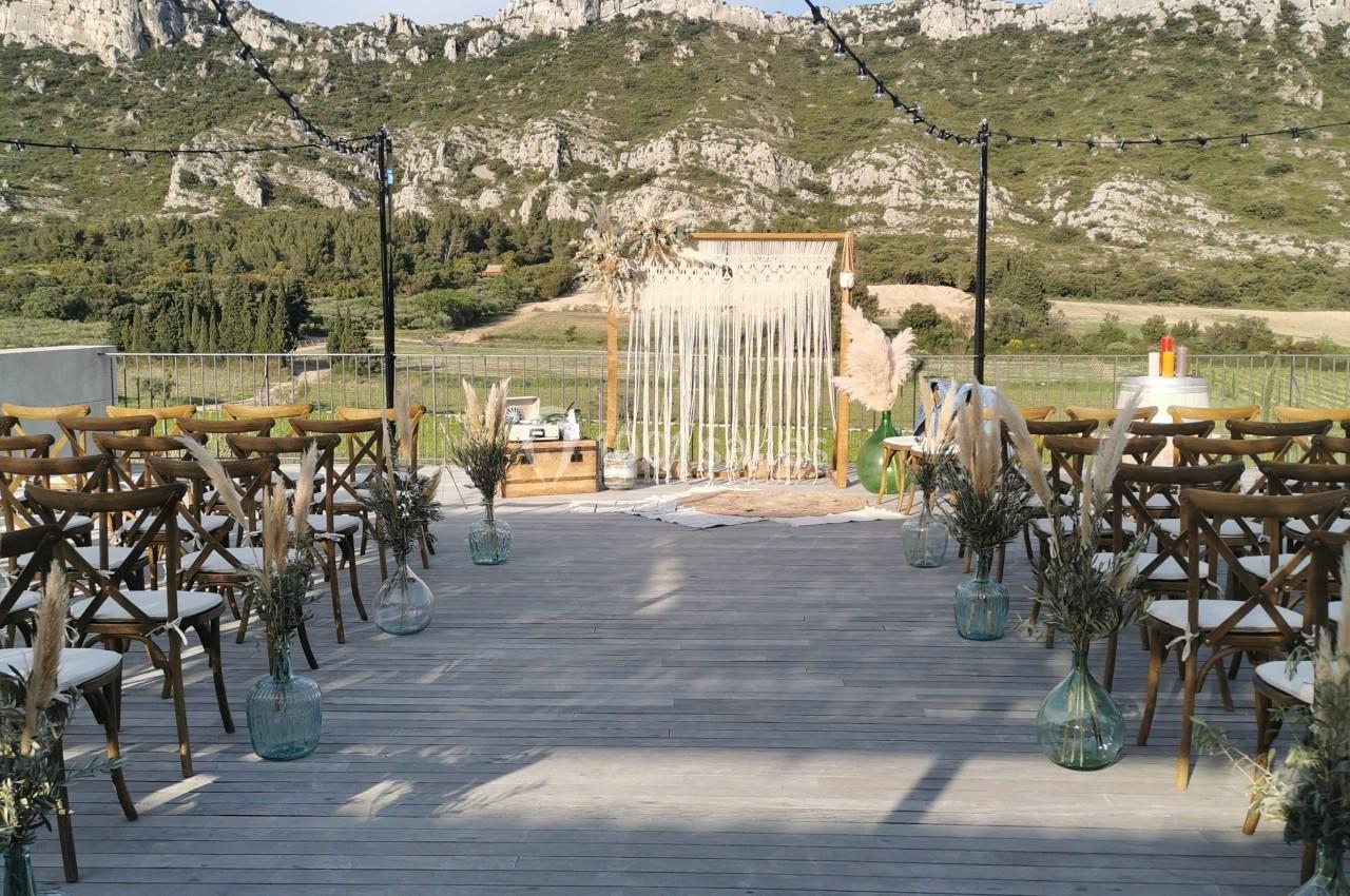 Allée en bois décorée pour une cérémonie en plein air, avec des chaises, des fleurs et une arche devant un paysage…
