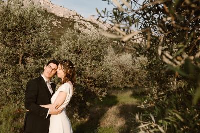 Un couple en tenue de mariage pose dans un champ d'oliviers sous une lumière douce.