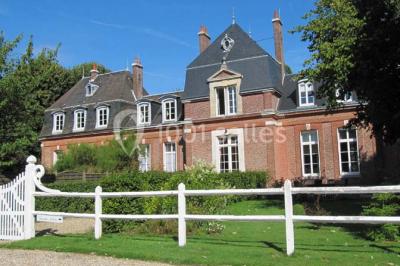Banc en bois sous une arche décorée de feuilles d'automne, entouré de bougies et de feuilles au sol dans une salle rustique.
