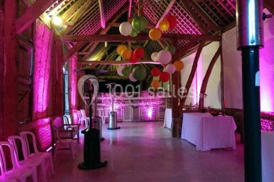 Banc en bois sous une arche décorée de feuilles d'automne, entouré de bougies et de feuilles au sol dans une salle rustique.