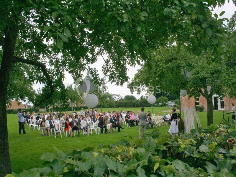Un groupe de personnes assises sur des chaises blanches lors d'une cérémonie en plein air dans un jardin verdoyant.