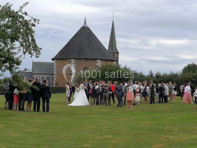 Groupe de personnes rassemblées sur une pelouse devant une église pour une cérémonie ou un événement festif.