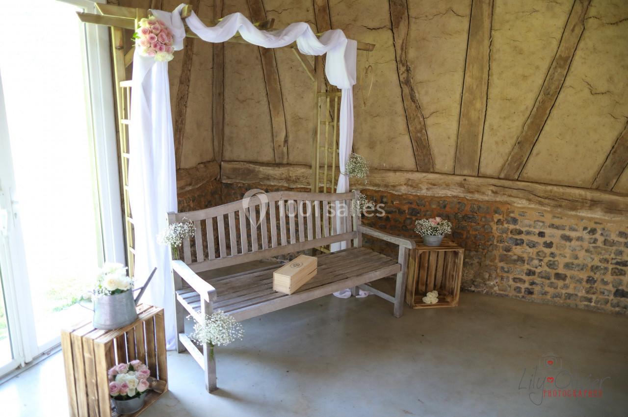 Banc en bois décoré de fleurs et de voilages blancs, placé dans un coin de mur en pierre et torchis.