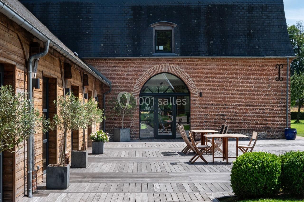 Cour en bois avec terrasse aménagée, chaises et table, entourée de bâtiments en briques et bois sous un ciel dégagé.