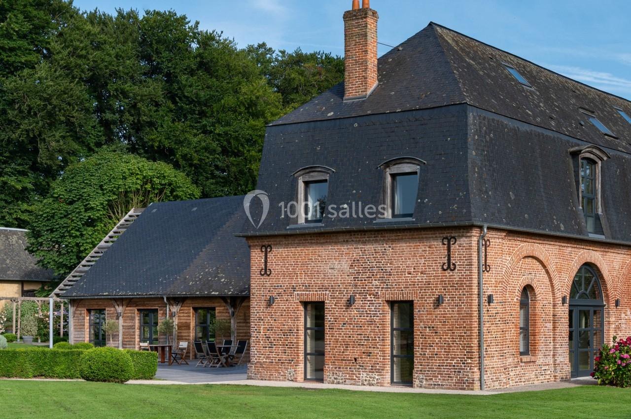Maison en briques rouges avec toit en ardoise, entourée de pelouse et bordée d'arbres sous un ciel bleu.