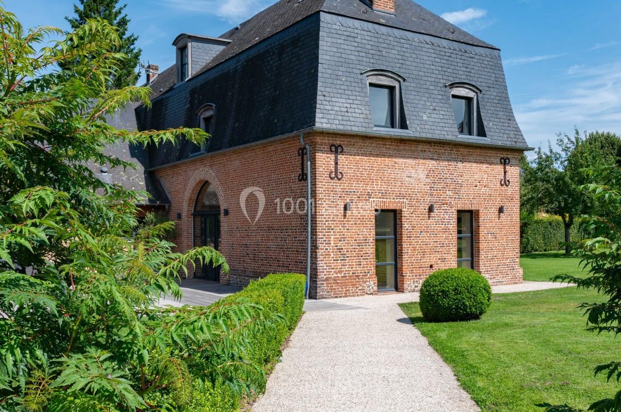 Maison en briques rouges avec toit en ardoise, entourée de verdure et d'une allée gravillonnée sous un ciel dégagé.
