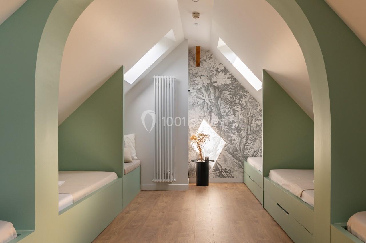 Chambre mansardée avec lits intégrés, murs verts, parquet clair et lumière naturelle provenant de fenêtres de toit.