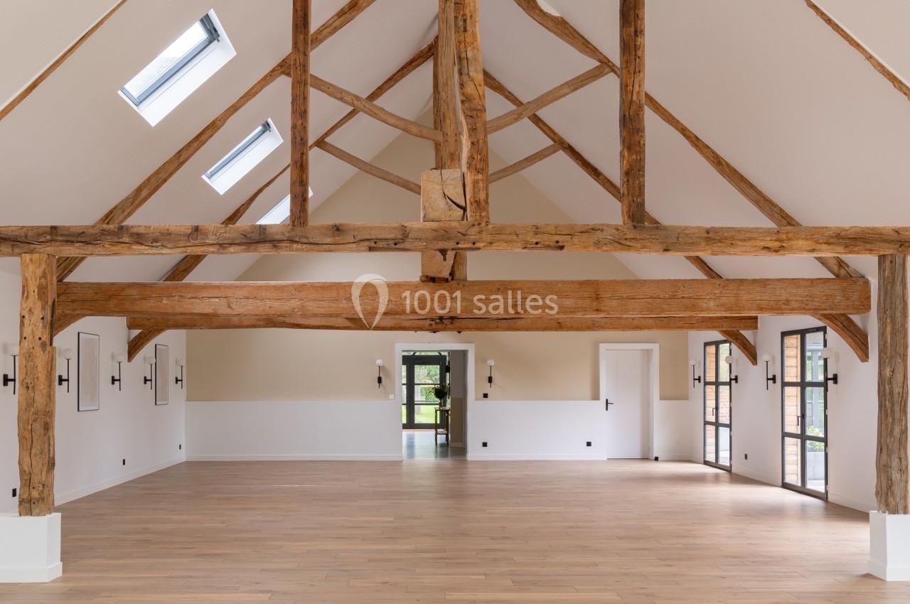 Grande pièce lumineuse avec poutres en bois apparentes, parquet clair et fenêtres laissant entrer la lumière naturelle.