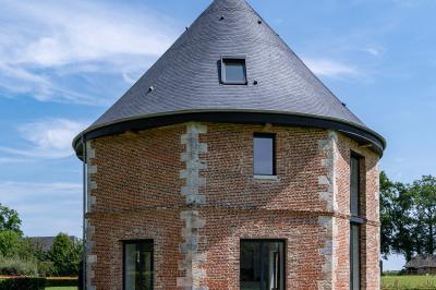 Banc en bois sous une arche décorée de feuilles d'automne, entouré de bougies et de feuilles au sol dans une salle rustique.