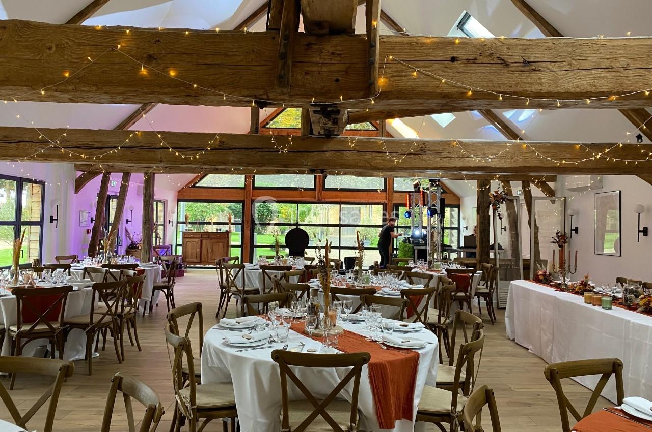 Salle de réception lumineuse avec poutres apparentes, tables dressées et décorations festives.