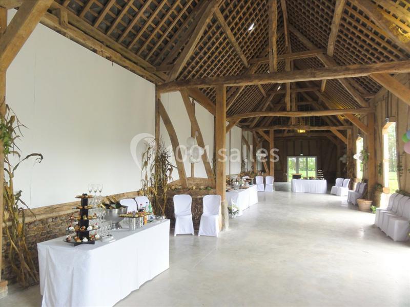 Salle de réception rustique avec poutres apparentes, tables dressées et décorations simples.
