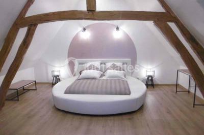 Lit double avec tête de lit sombre, draps gris et blancs, encadré par deux tables de chevet avec lampes, dans une chambre…