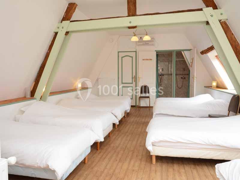 Chambre mansardée avec cinq lits simples, poutres apparentes, sol en bois et salle de bain attenante.