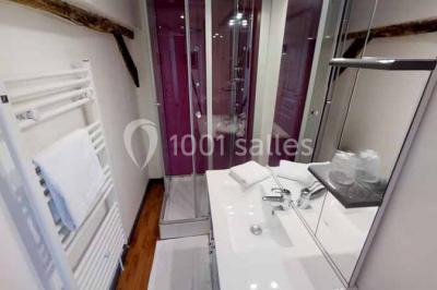 Lit double avec tête de lit sombre, draps gris et blancs, encadré par deux tables de chevet avec lampes, dans une chambre…