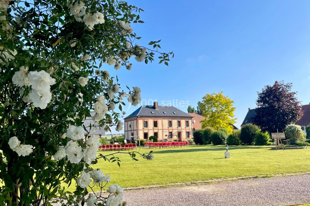 Vue d'une maison en briques entourée d'un jardin verdoyant, avec des fleurs blanches au premier plan.