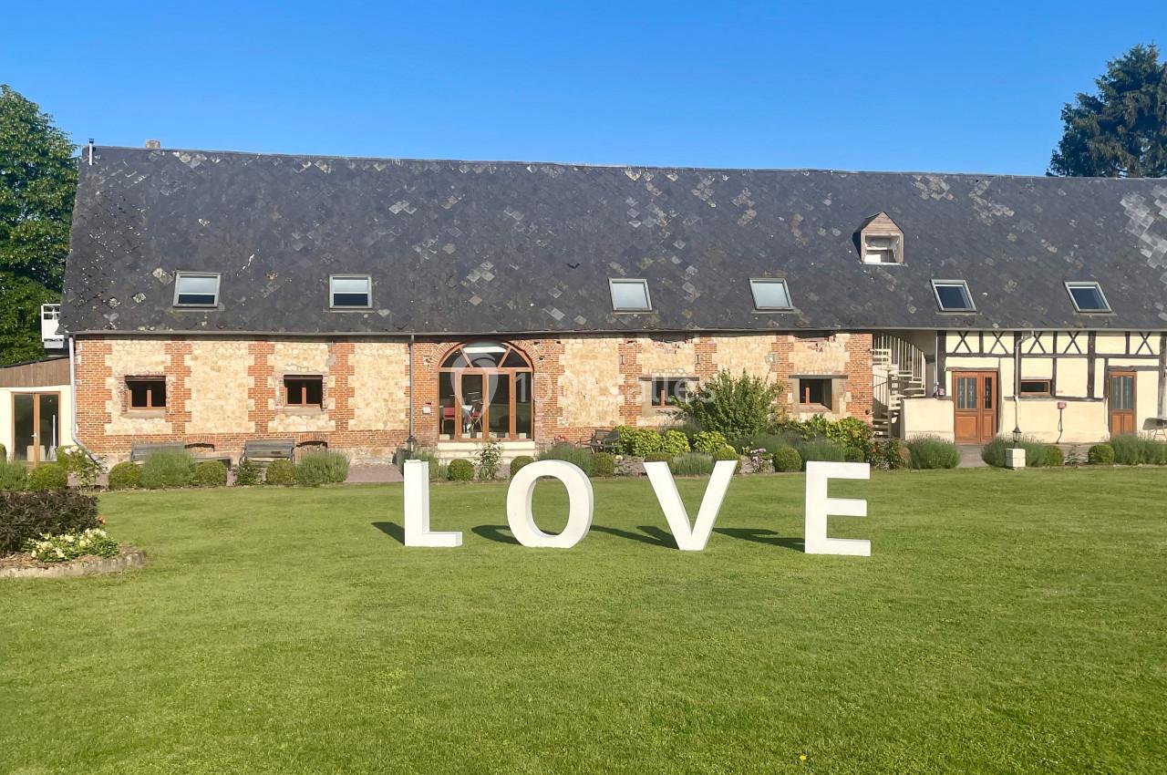 Grand bâtiment en briques et colombages avec pelouse verte, décoré de grandes lettres blanches formant le mot ’LOVE’.