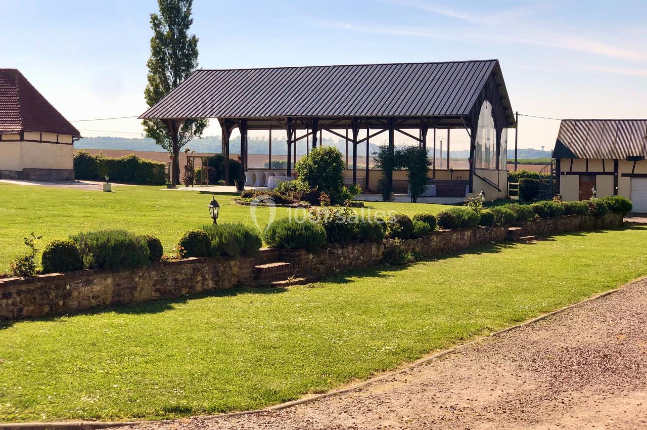 Abri en bois ouvert entouré de pelouses bien entretenues, avec des bâtiments ruraux en arrière-plan.