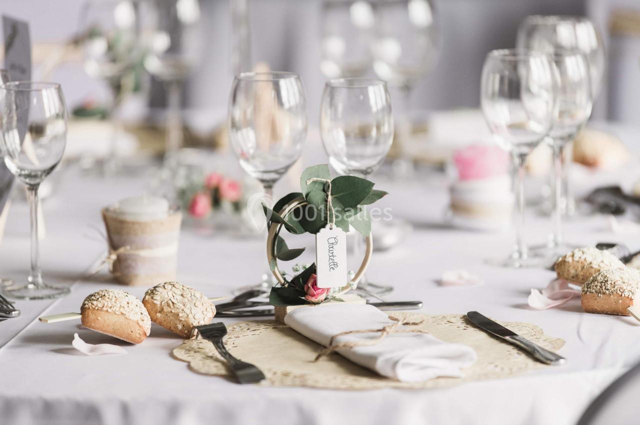 Table dressée avec des verres, couverts, petits pains et une décoration florale au centre.