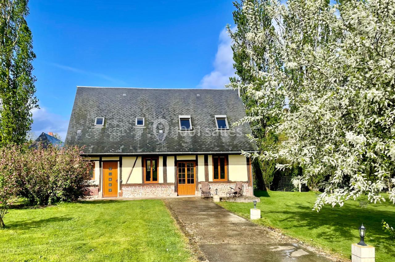 Maison à colombages entourée d'arbres en fleurs et d'une pelouse, avec une allée pavée menant à l'entrée.