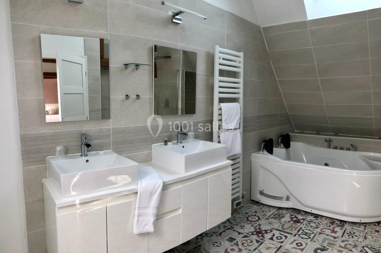 Salle de bain moderne avec double vasque, baignoire d'angle, sèche-serviettes et carrelage décoratif au sol.