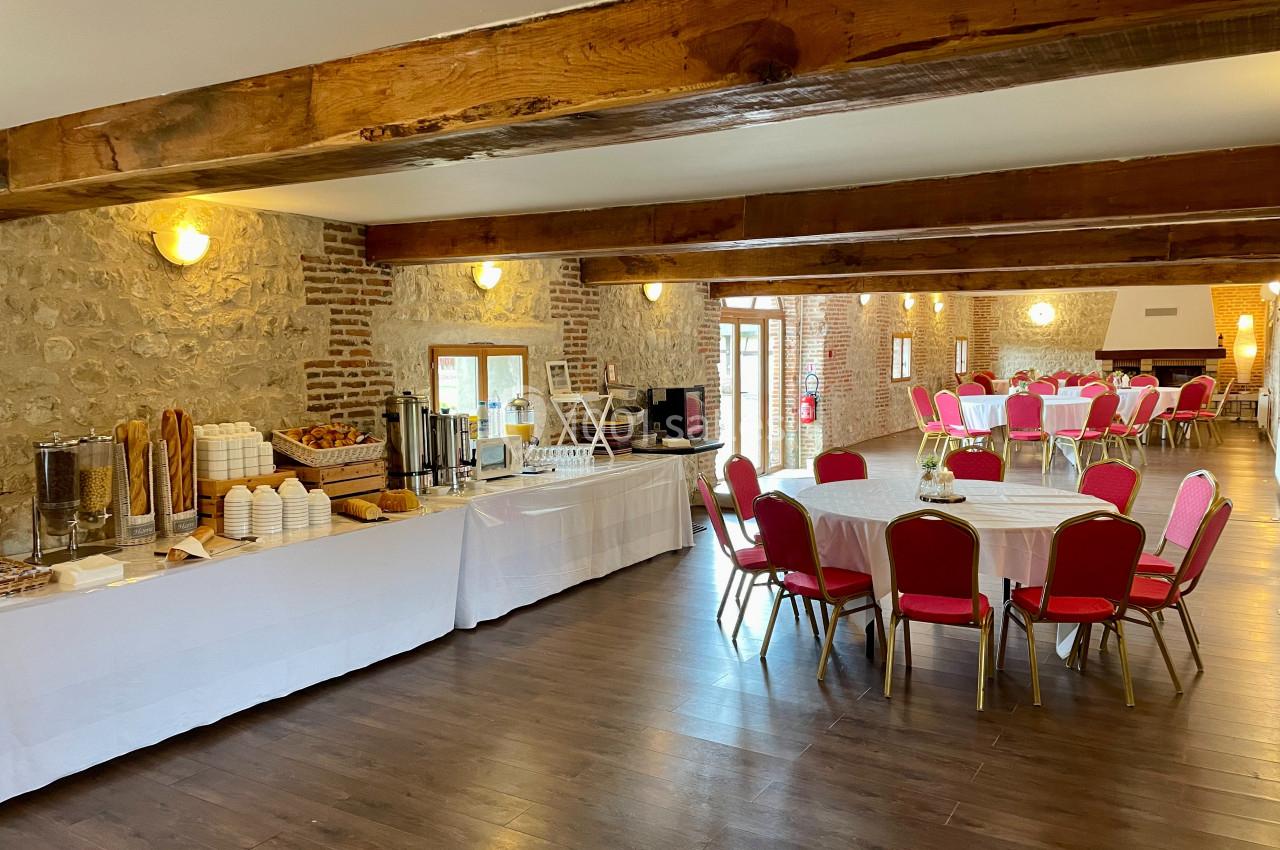 Salle de réception avec tables rondes dressées et buffet installé le long d'un mur en pierre apparente.
