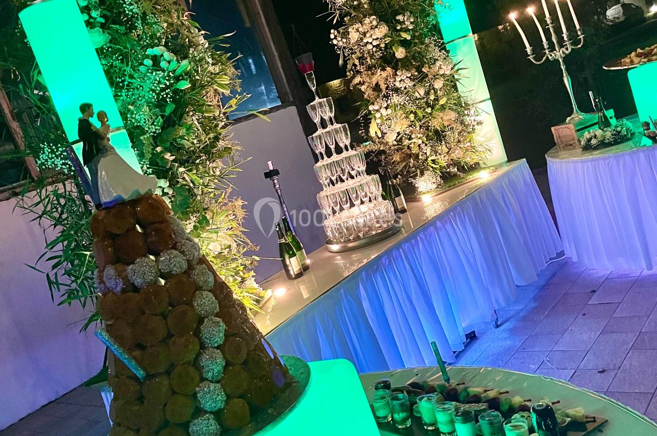 Pièce montée éclairée en vert devant une pyramide de coupes et des décorations florales dans une salle de réception.