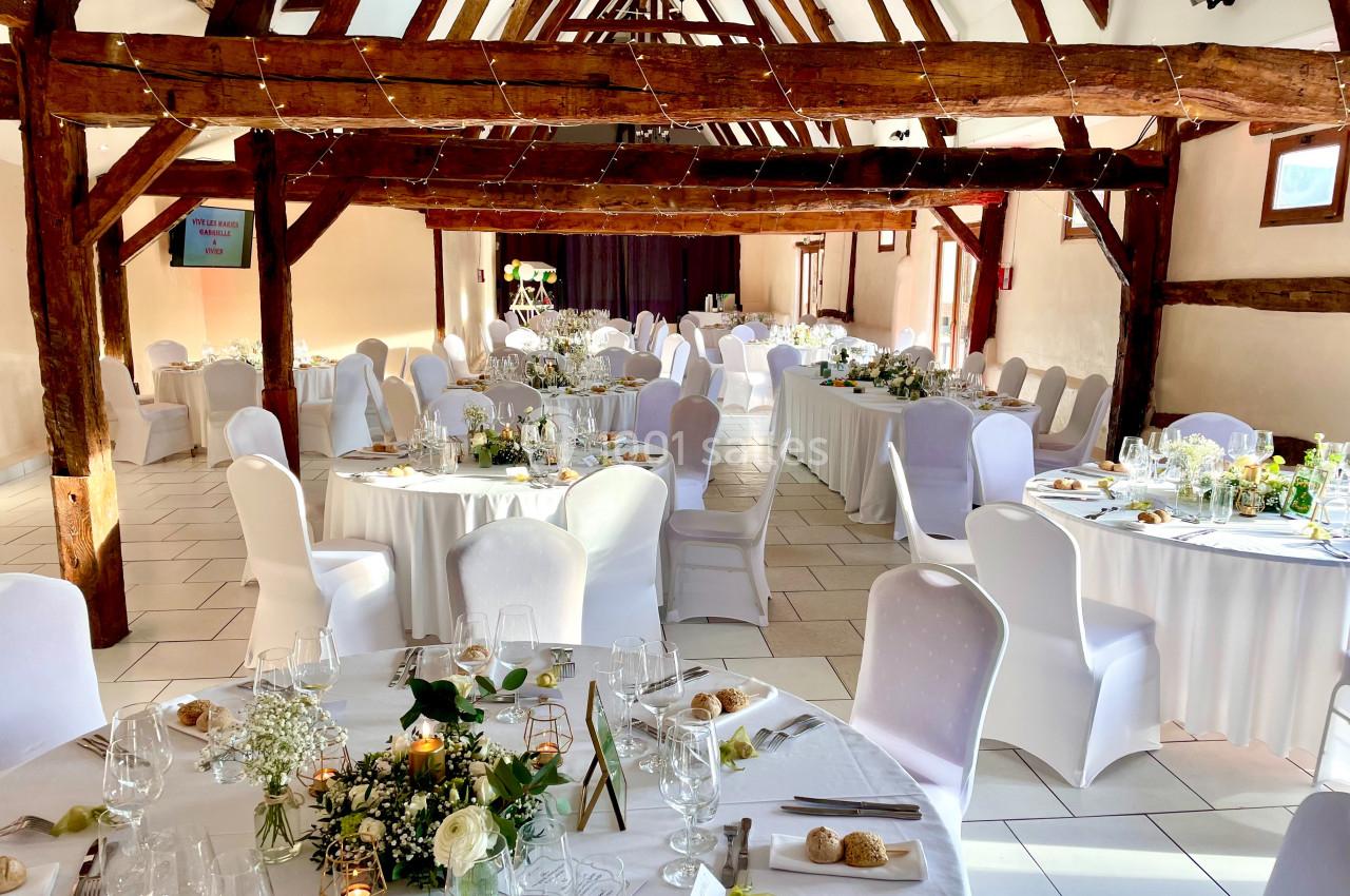 Salle de réception lumineuse avec tables rondes et rectangulaires décorées pour un événement festif.