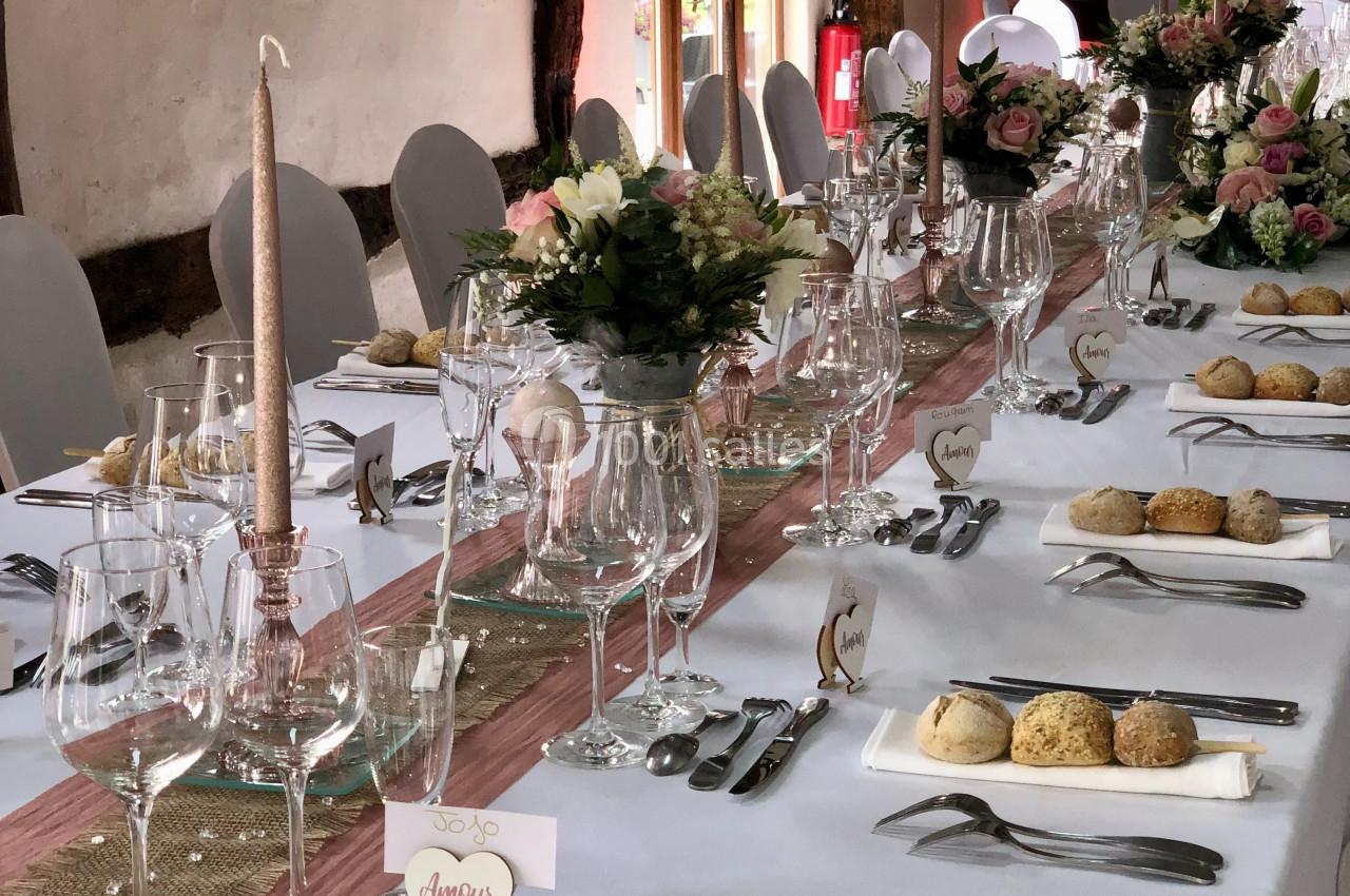 Table de réception élégamment dressée avec nappes blanches, bouquets de fleurs, verres, couverts et petits pains.