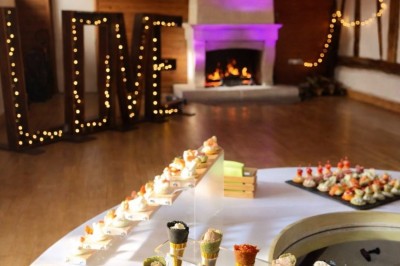 Table garnie de pâtisseries, macarons, fruits et biscuits, disposée en extérieur avec un jardin en arrière-plan.