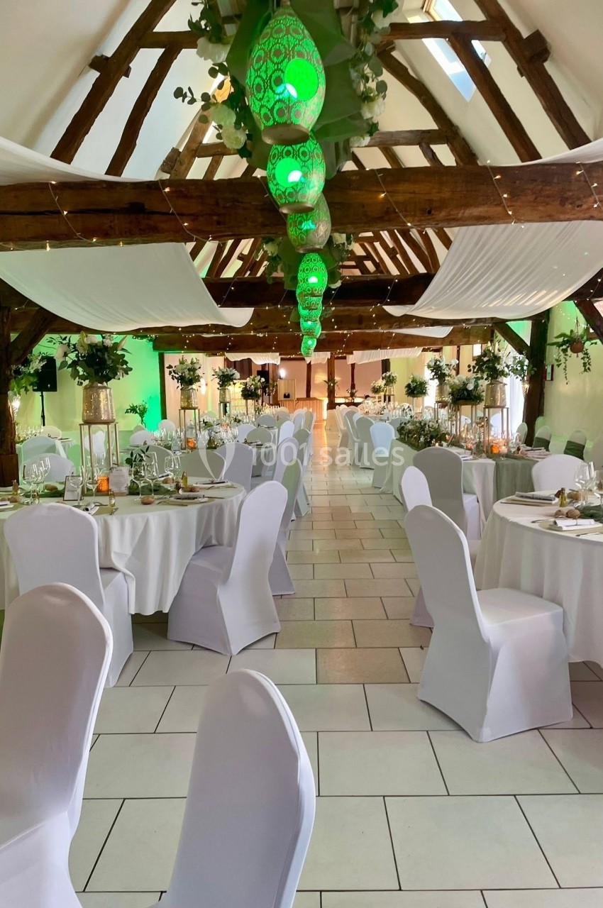 Salle de réception décorée avec des tables rondes, chaises blanches et lanternes vertes suspendues au plafond en bois.