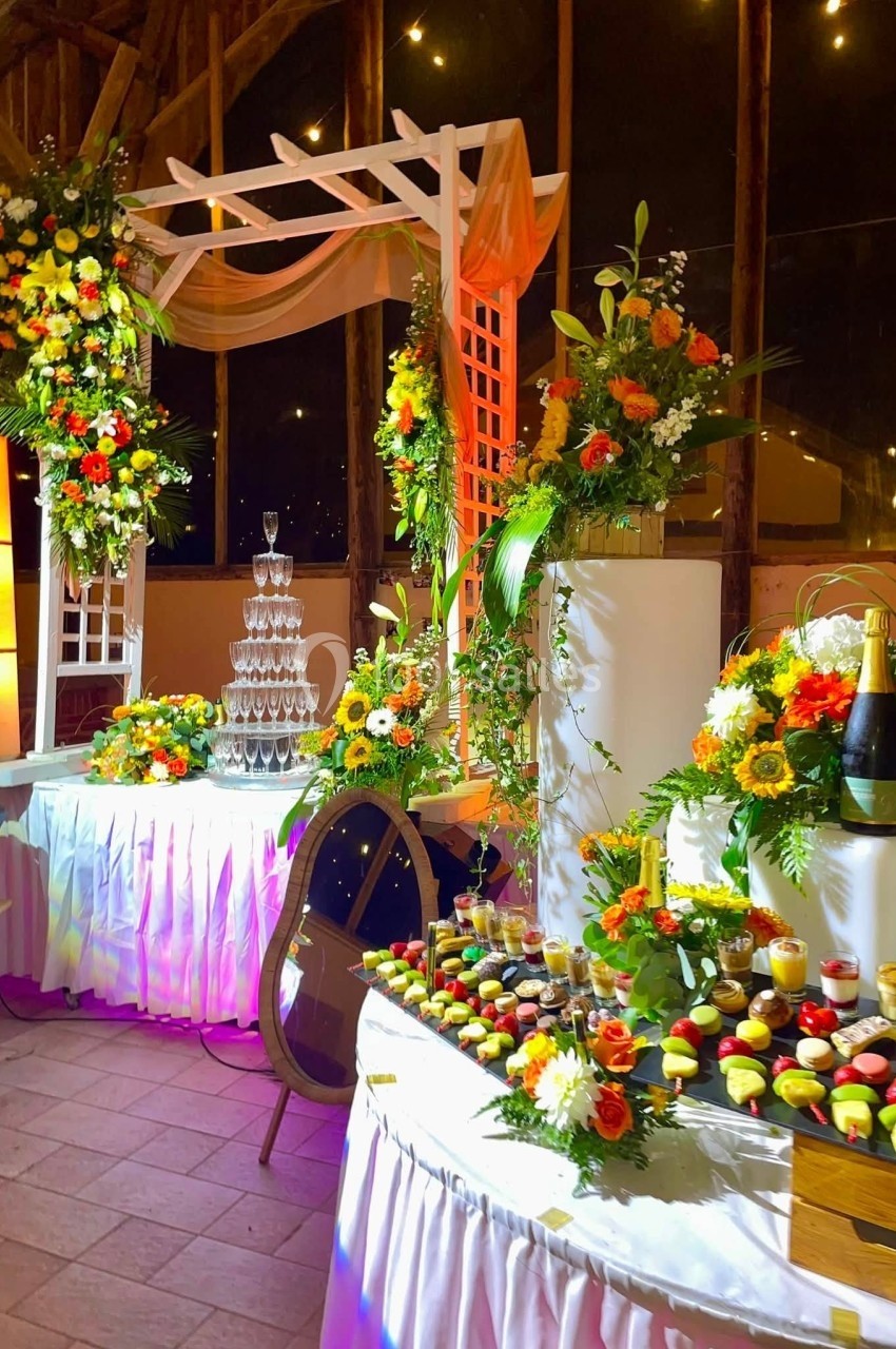 Location salle Argueil (Seine-Maritime) - Domaine de Clairval #20 Buffet décoré avec des fleurs colorées, une pyramide de flûtes à champagne et des desserts variés sur des tables éclairées.