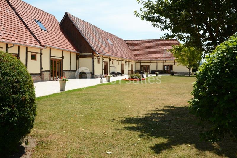 Bâtiments à toit en tuiles rouges entourés d'une cour en pelouse et d'arbres sous un ciel dégagé.