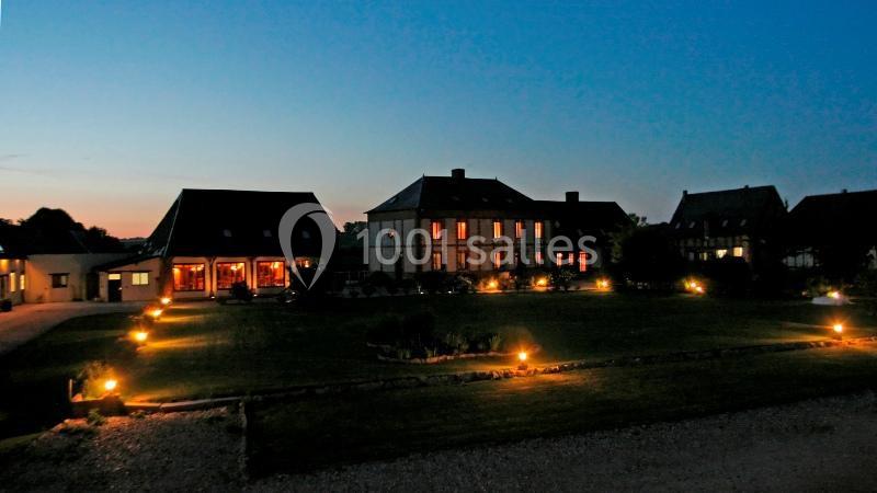 Bâtiments éclairés par des lumières extérieures dans un grand jardin au crépuscule.