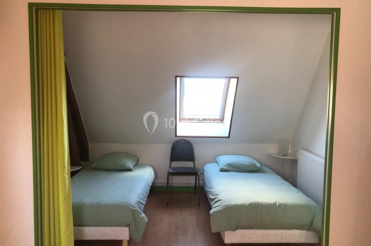 Deux lits simples avec draps verts dans une chambre mansardée, éclairée par une fenêtre de toit.